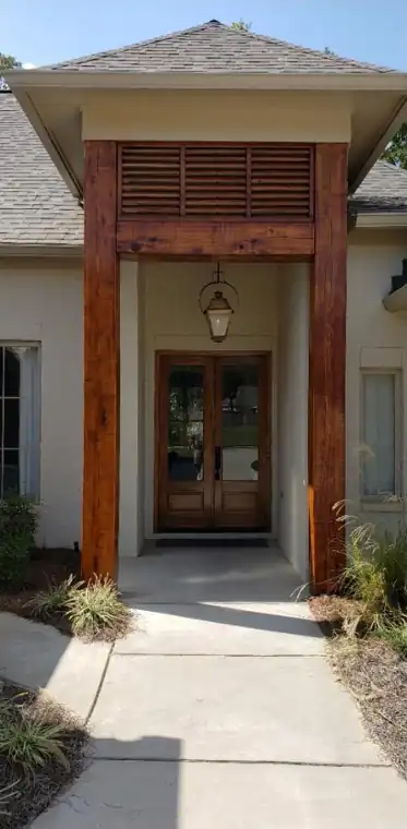 Double wooden entry doors under a tall timber-clad portico, freshly stained