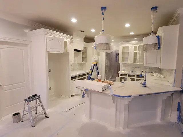 Kitchen with cabinets freshly painted white, pendant lights bagged and the island edge taped
