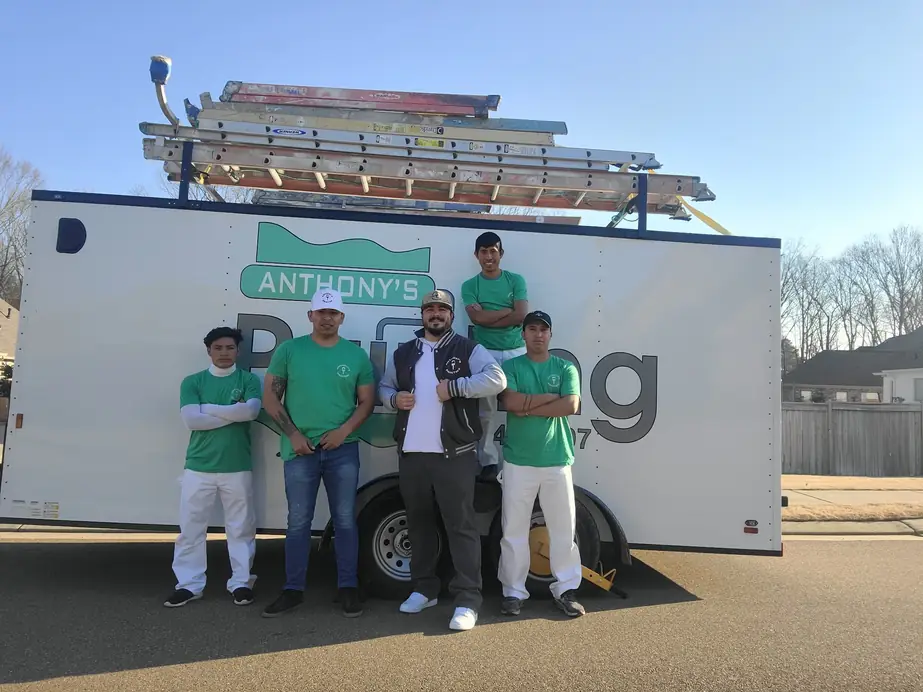 Anthony's Painting crew in green shirts standing in front of the company trailer, ladders racked on top